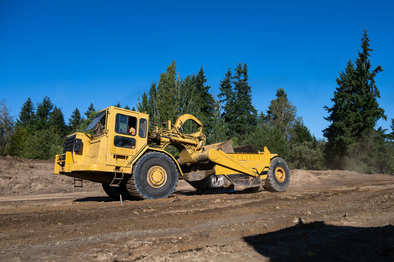 Wheel Tractor Scraper moving mineral dirt and working on groundwork for new housing development project, leveling ground for road works, as a construction background