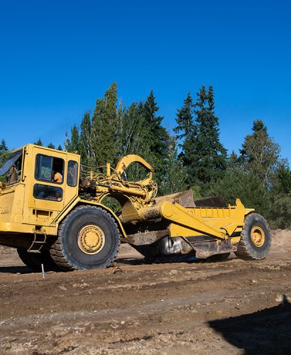 Wheel Tractor Scraper moving mineral dirt and working on groundwork for new housing development project, leveling ground for road works, as a construction background